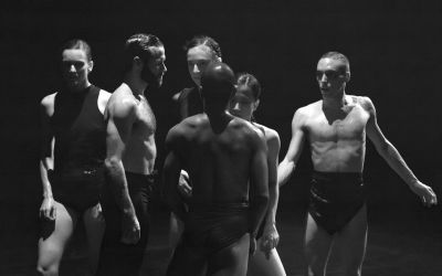 czarno-białe zdjęcie grupa artystów patrzy w różne strony na siebie nawzajem, czarne stroje, czarne tło