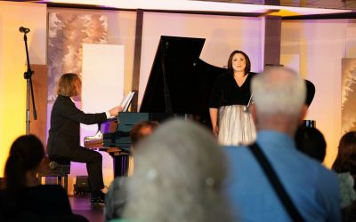 śpiewająca Joanna Rot i grający na fortepianie Michał Rot na żółtym tle, zdjęcie z perspektywy widowni