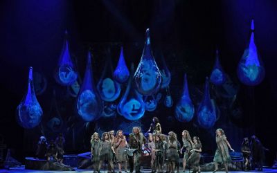 scena zbiorowa, artyści ubrani w zgniłozielone stroje, niebieskie tło z którego spadają duże niebieskie krople, w środku kropel jasne kształty